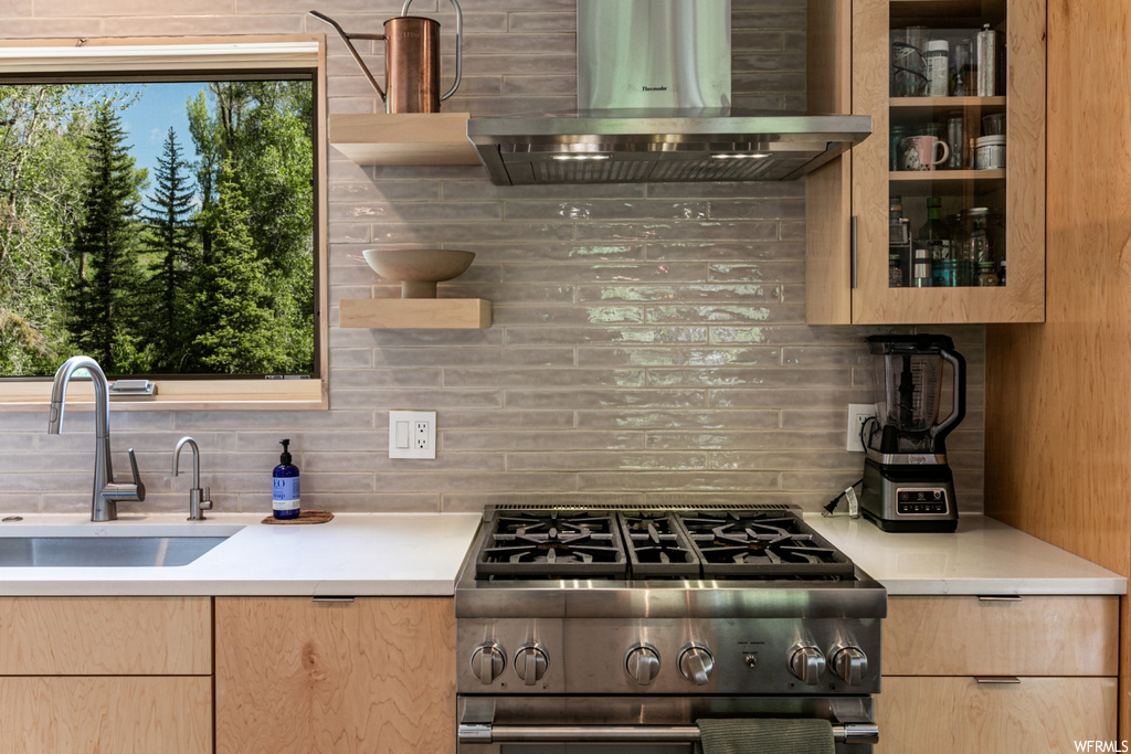 Kitchen featuring wall chimney exhaust hood, backsplash, high end stainless steel range oven, and light countertops