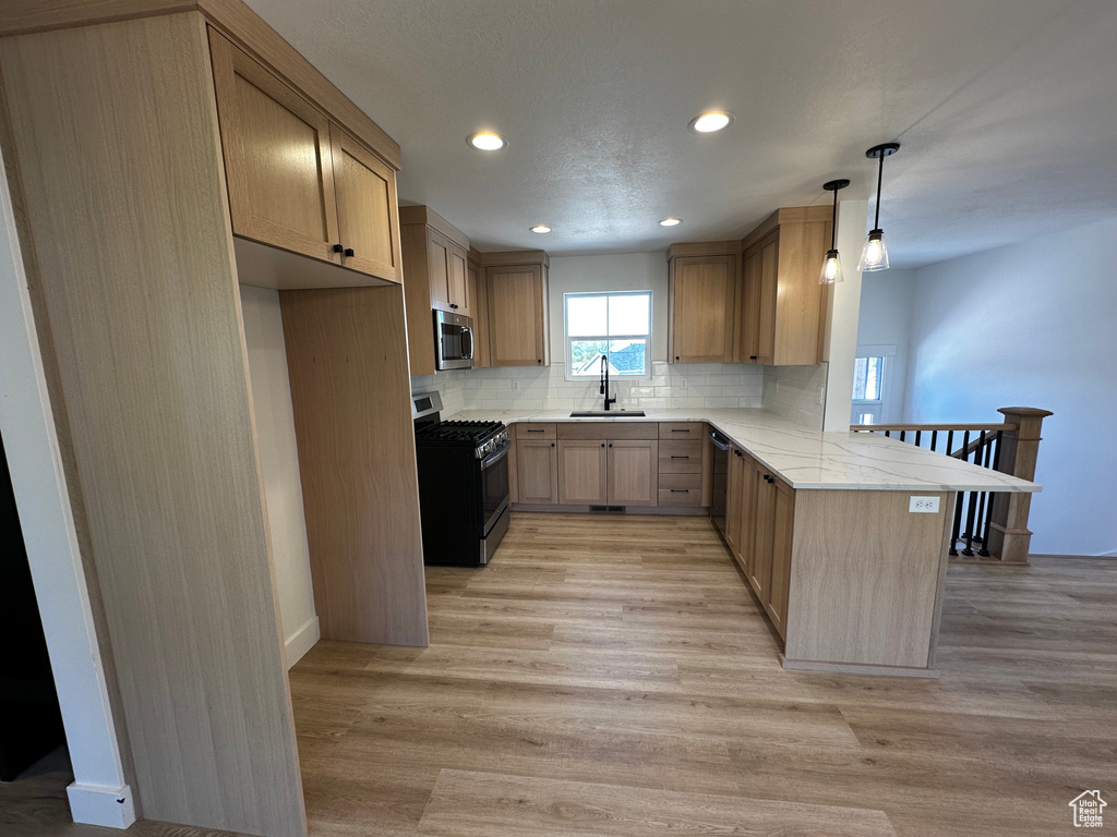 Kitchen featuring gas range, sink, light hardwood / wood-style floors, backsplash, and kitchen peninsula