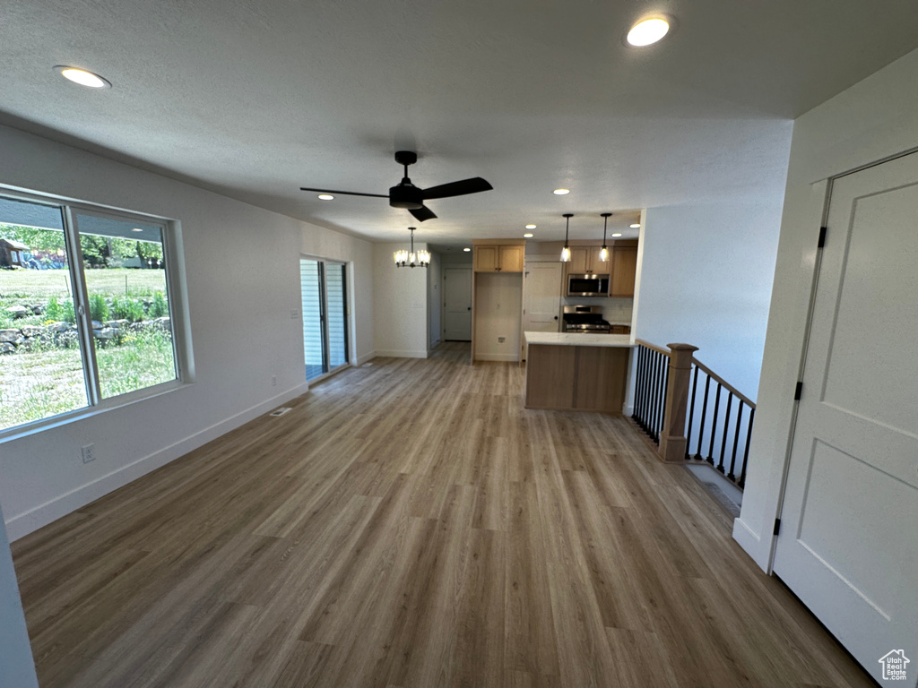 Unfurnished living room featuring hardwood / wood-style flooring and ceiling fan with notable chandelier