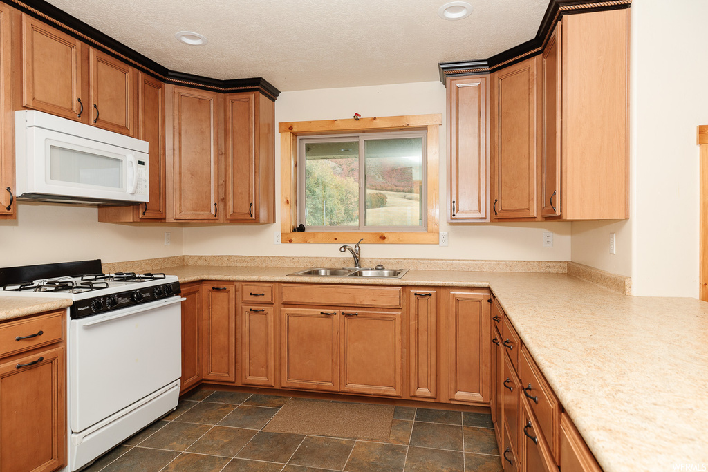Kitchen featuring sink, white appliances, and dark tile flooring