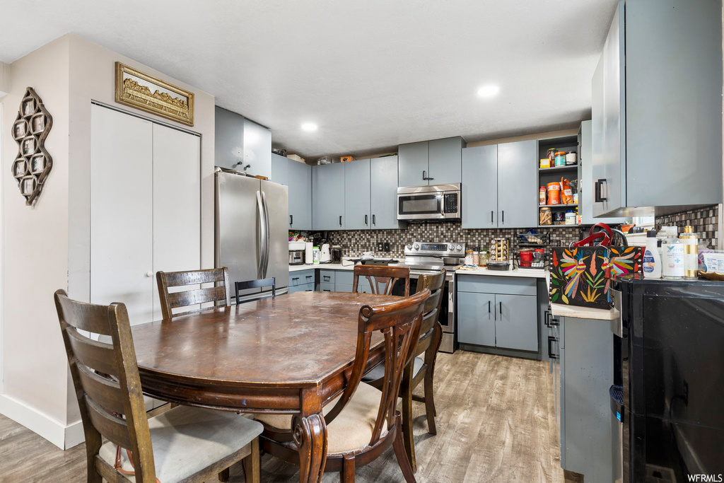 Kitchen with tasteful backsplash, gray cabinets, light hardwood floors, and appliances with stainless steel finishes