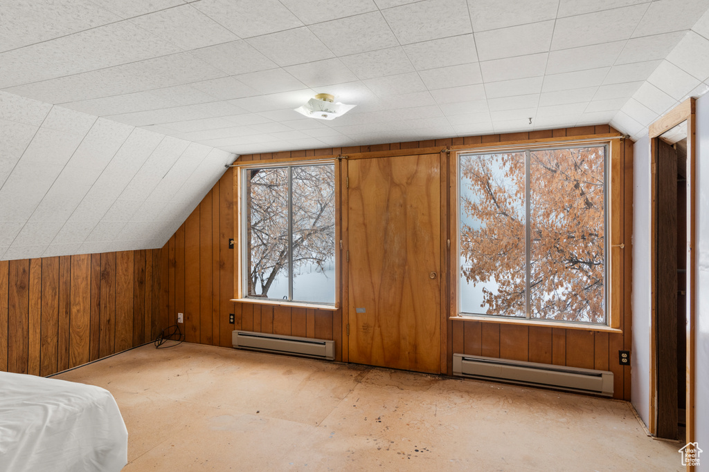 Additional living space with wood walls, a baseboard heating unit, and lofted ceiling