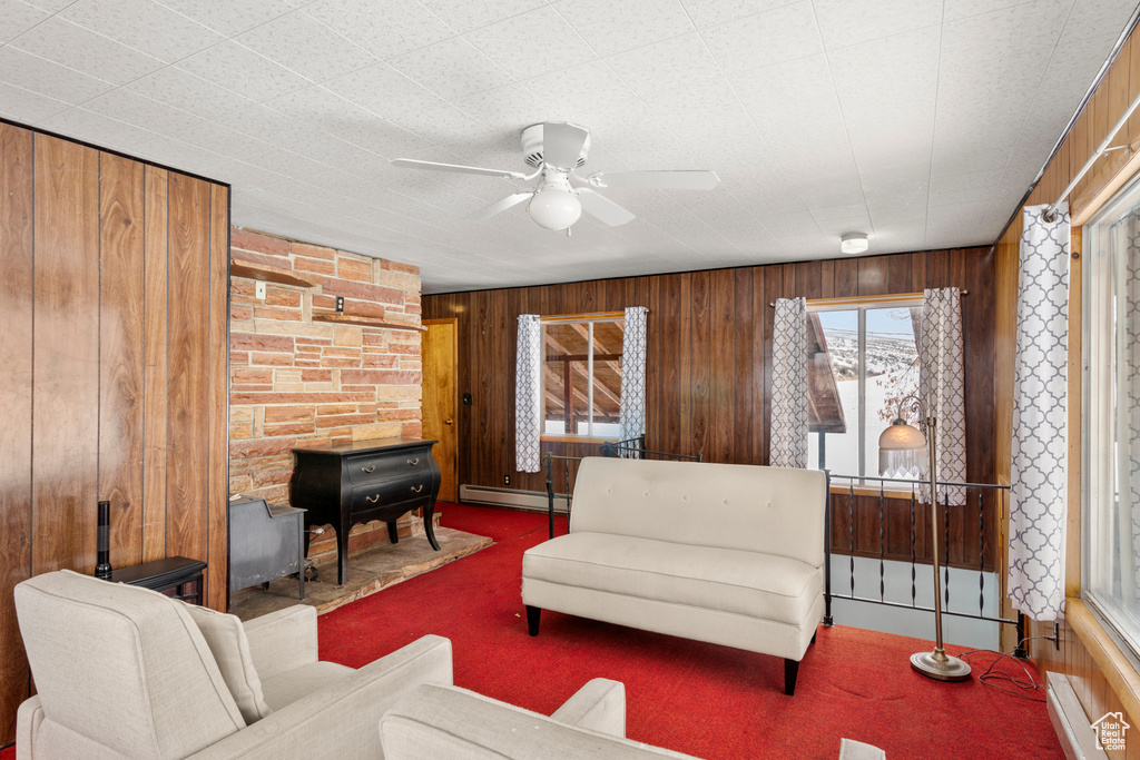 Living room featuring dark carpet, wood walls, a baseboard heating unit, and ceiling fan