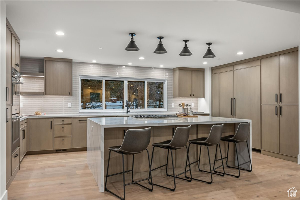 Kitchen featuring backsplash, light hardwood / wood-style flooring, pendant lighting, and a center island