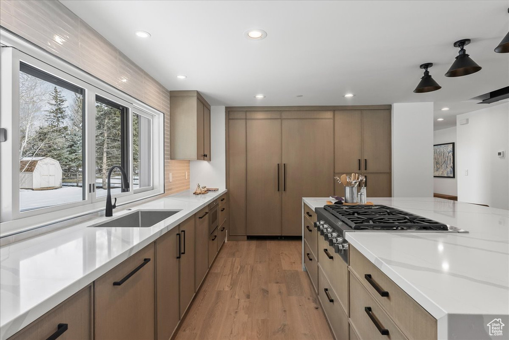Kitchen with sink, light stone countertops, tasteful backsplash, decorative light fixtures, and light wood-type flooring