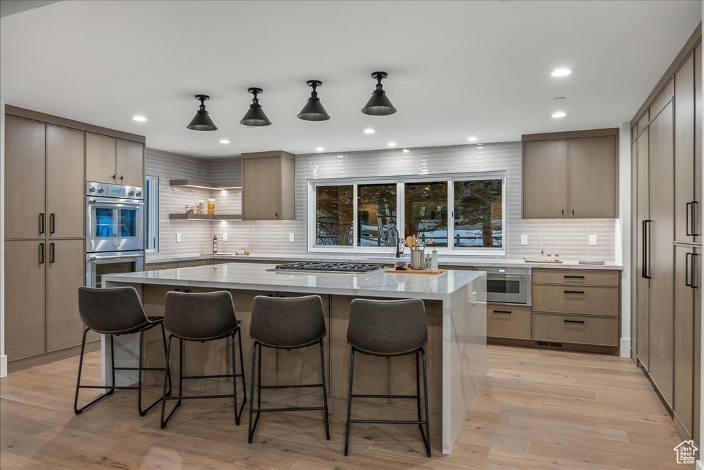 Kitchen featuring hanging light fixtures, appliances with stainless steel finishes, a center island, tasteful backsplash, and light wood-type flooring