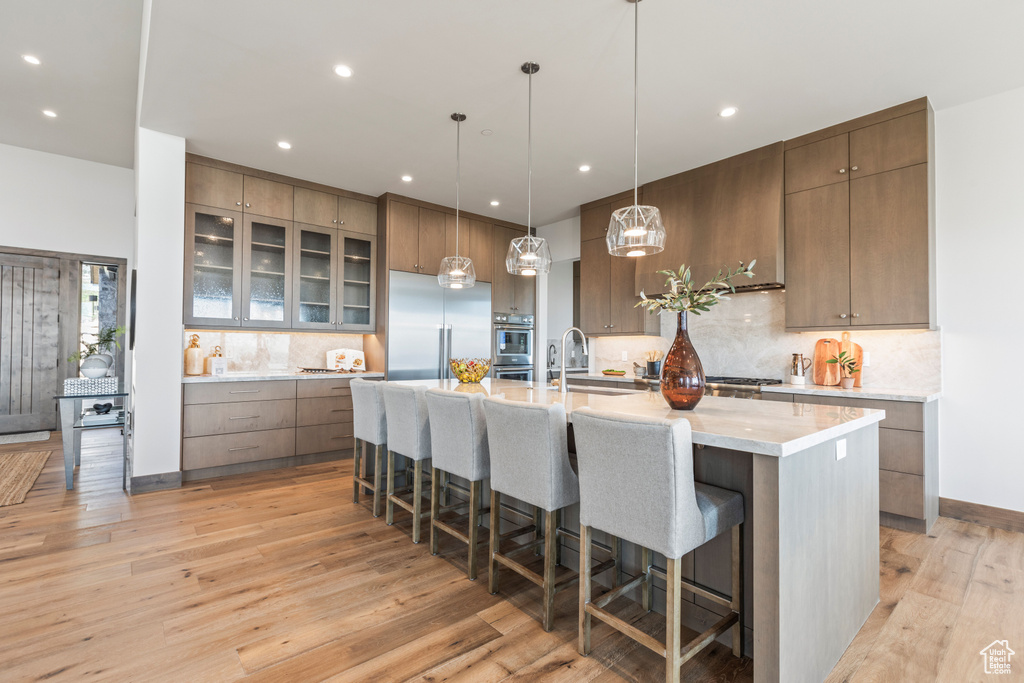 Kitchen featuring a kitchen breakfast bar, a kitchen island with sink, light hardwood / wood-style flooring, backsplash, and appliances with stainless steel finishes