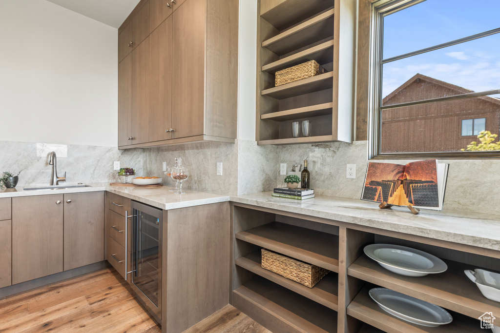Kitchen with beverage cooler, sink, backsplash, light wood-type flooring, and light stone countertops