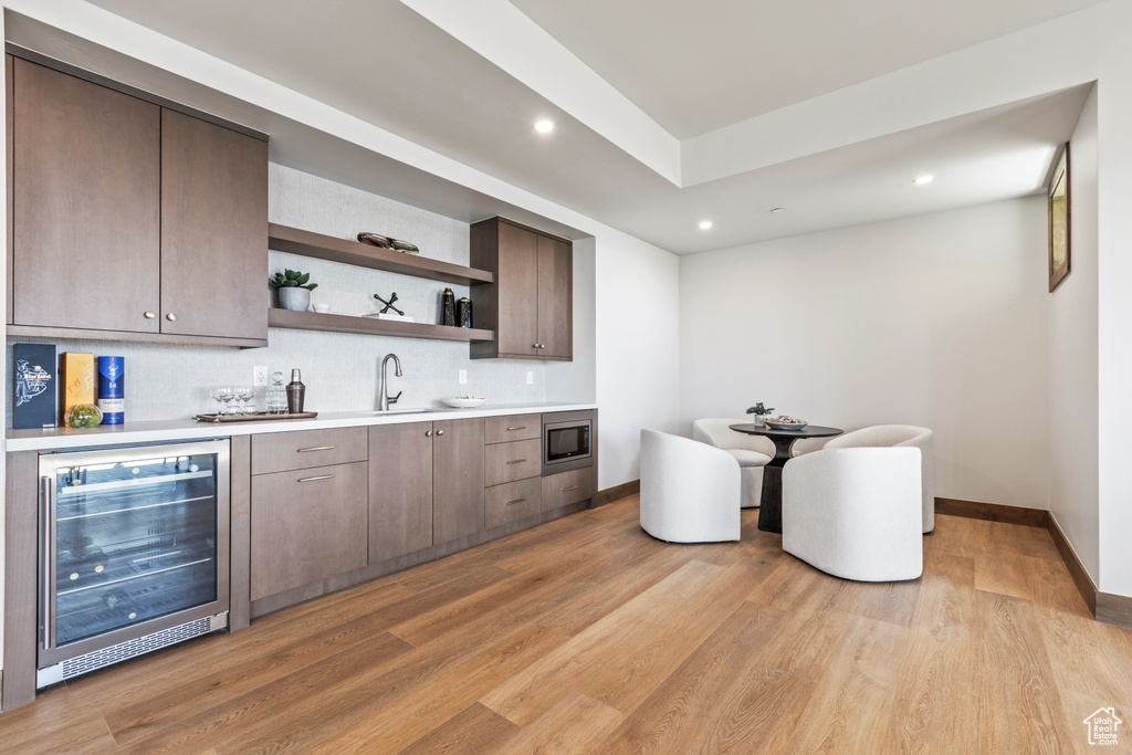 Kitchen with backsplash, light hardwood / wood-style flooring, stainless steel microwave, wine cooler, and sink