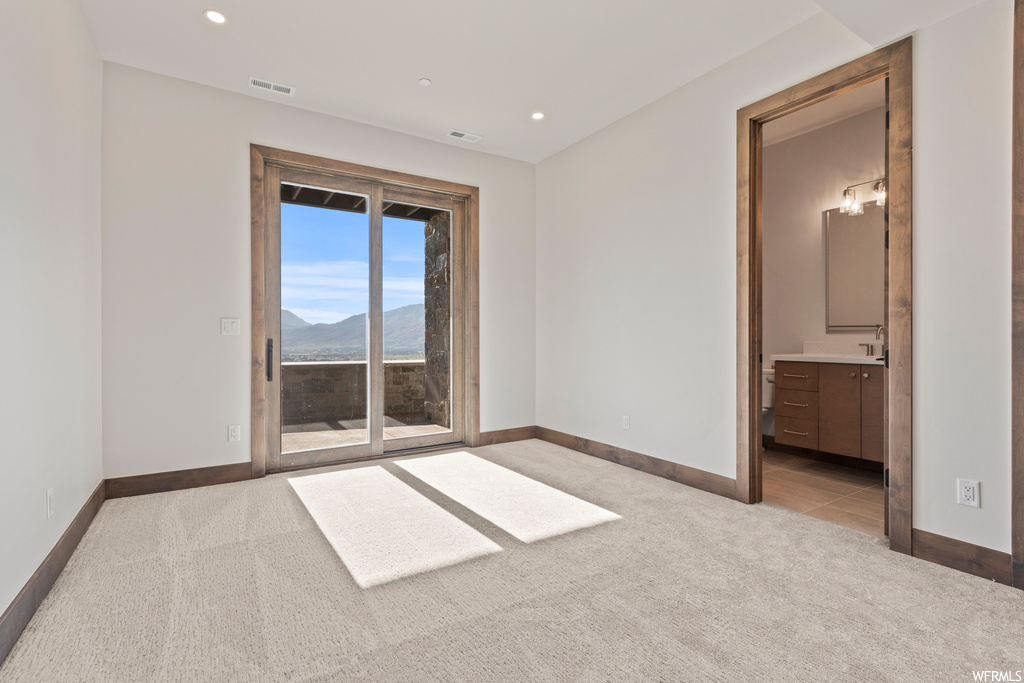 Unfurnished bedroom with light carpet, access to exterior, ensuite bath, and a mountain view