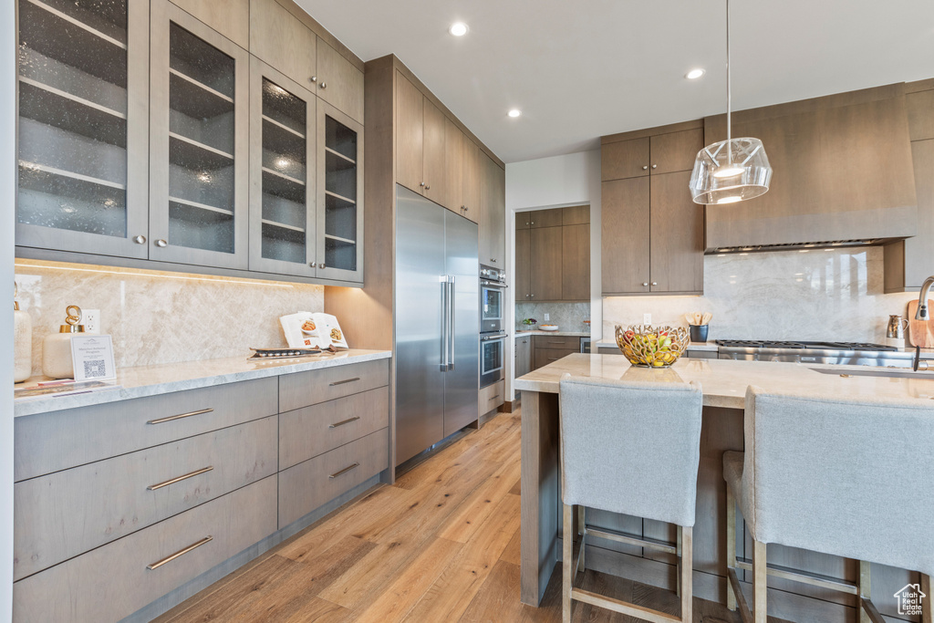 Kitchen featuring hanging light fixtures, light hardwood / wood-style floors, backsplash, and appliances with stainless steel finishes