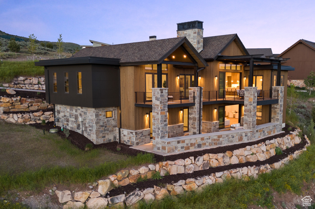 Back house at dusk with a pergola and a balcony