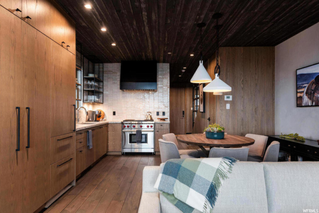 Kitchen featuring dark hardwood flooring, wooden walls, hanging light fixtures, designer range, and exhaust hood