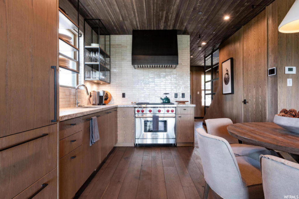Kitchen with tasteful backsplash, dark hardwood flooring, light stone counters, wall chimney exhaust hood, and sink