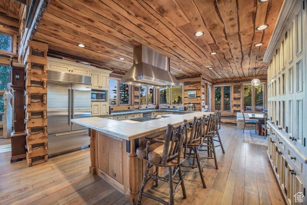Kitchen with light hardwood / wood-style floors, decorative light fixtures, wooden ceiling, island exhaust hood, and built in appliances