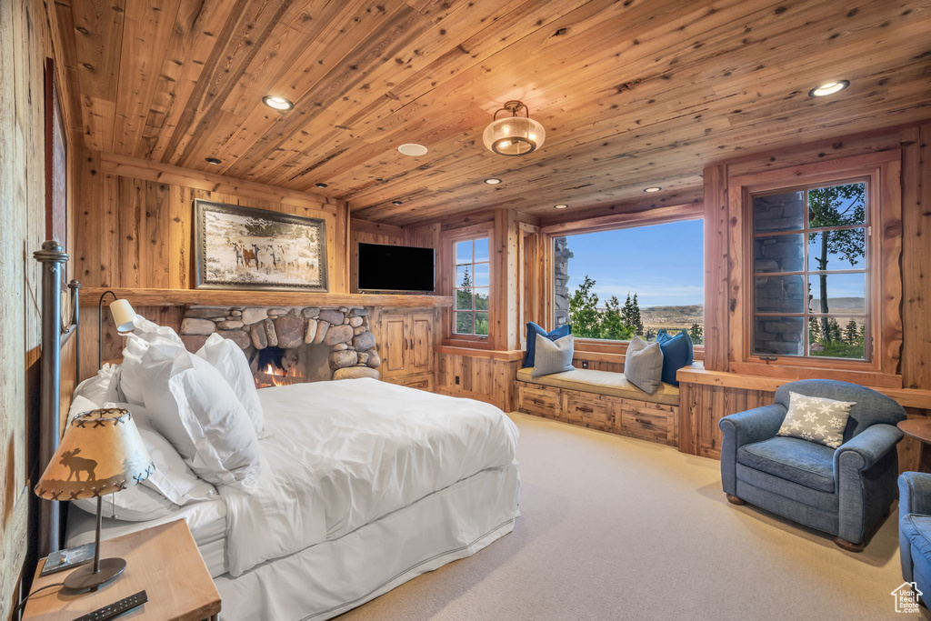 Carpeted bedroom with wooden walls, a stone fireplace, and wood ceiling