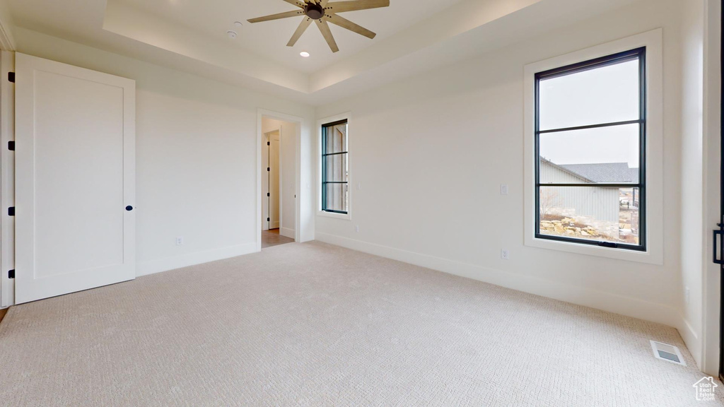 Empty room featuring light carpet, a tray ceiling, and ceiling fan
