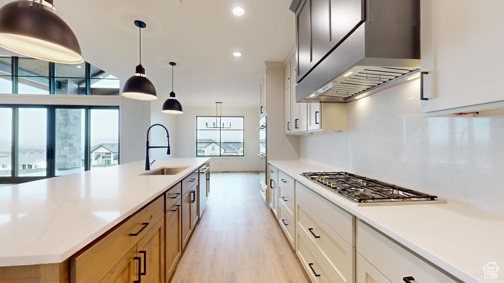 Kitchen featuring a kitchen island with sink, light hardwood / wood-style floors, sink, wall chimney exhaust hood, and pendant lighting