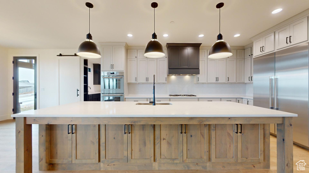 Kitchen with pendant lighting, tasteful backsplash, stainless steel appliances, and a center island with sink