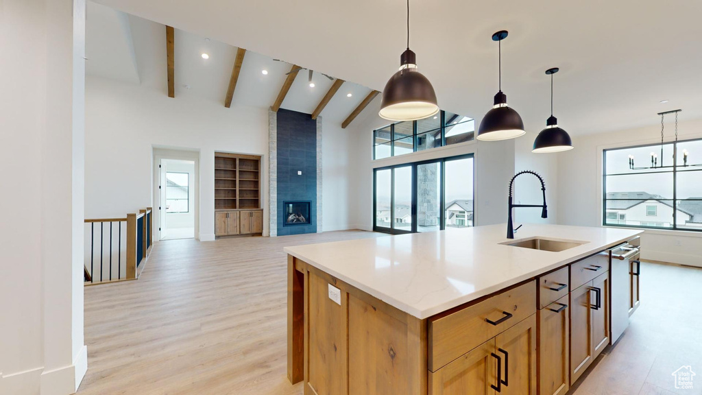 Kitchen with an island with sink, pendant lighting, light hardwood / wood-style floors, beam ceiling, and sink