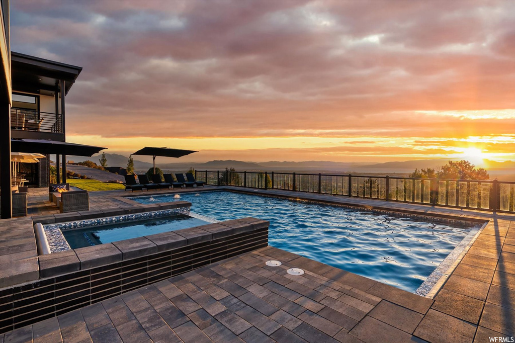 Pool at dusk featuring an in ground hot tub and a patio area