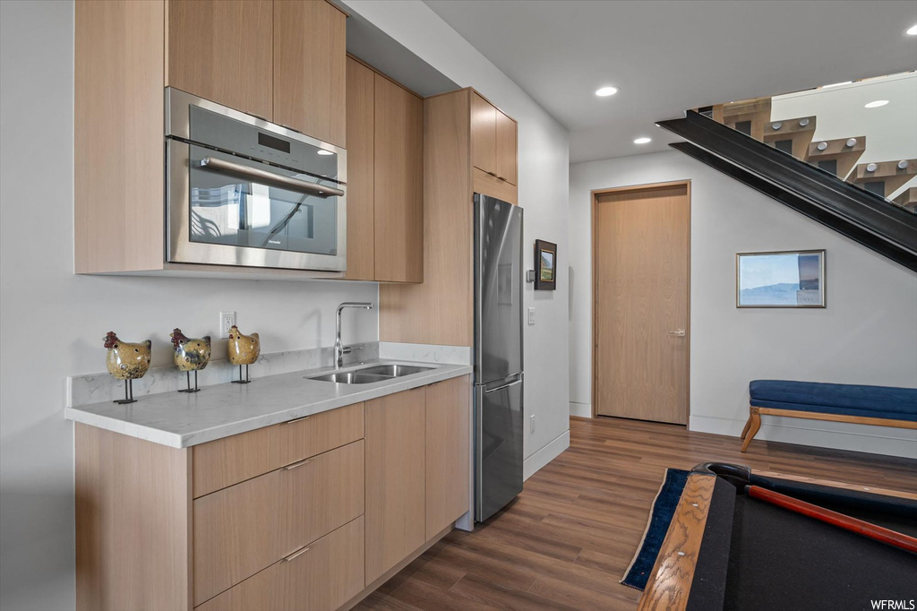 Kitchen with dark hardwood flooring, sink, light brown cabinets, and stainless steel fridge
