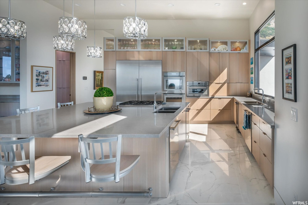 Kitchen featuring sink, pendant lighting, a notable chandelier, a kitchen island with sink, and light tile flooring