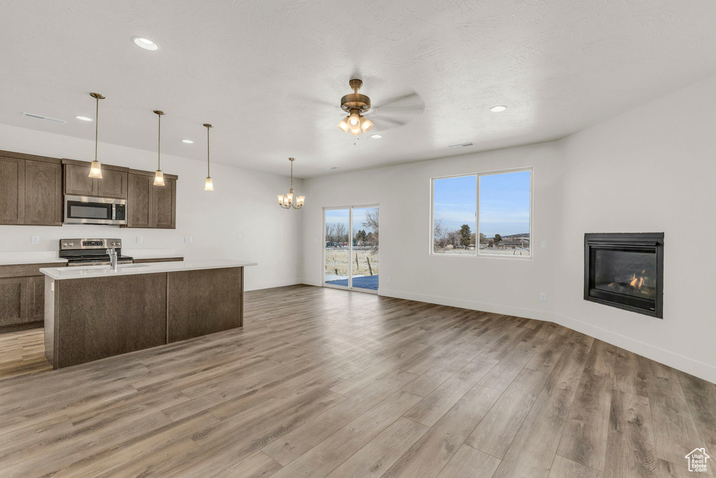 Kitchen featuring light hardwood / wood-style flooring, hanging light fixtures, stainless steel appliances, and ceiling fan with notable chandelier