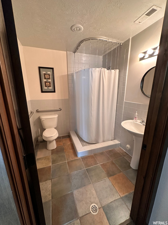 Bathroom featuring sink, toilet, a textured ceiling, a shower with curtain, and tile walls