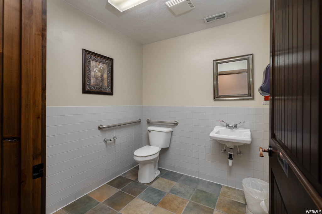 Bathroom with tile floors, toilet, tile walls, and sink