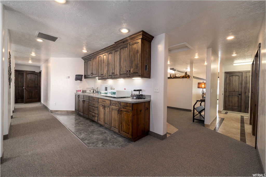 Kitchen featuring sink, dark carpet, dark brown cabinets, and a textured ceiling