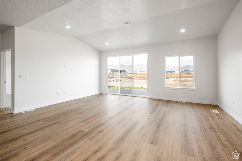 Empty room featuring light hardwood / wood-style floors, lofted ceiling, and a healthy amount of sunlight