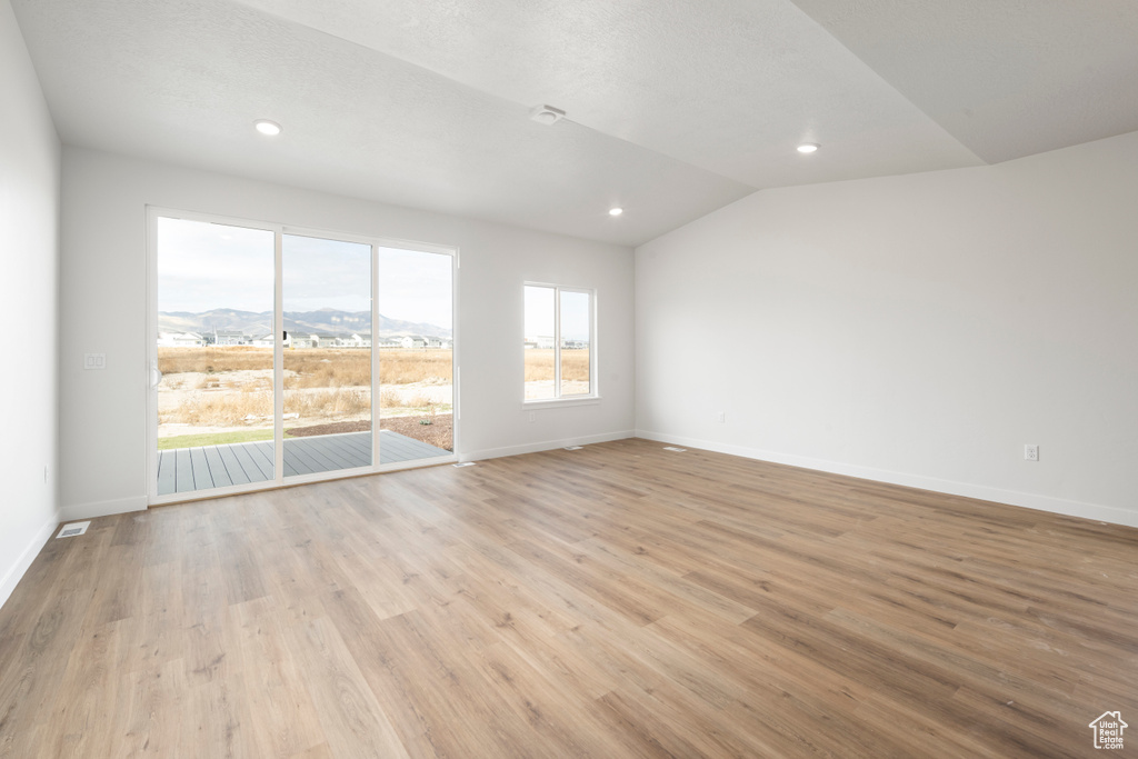 Unfurnished room with light hardwood / wood-style floors, lofted ceiling, and a mountain view