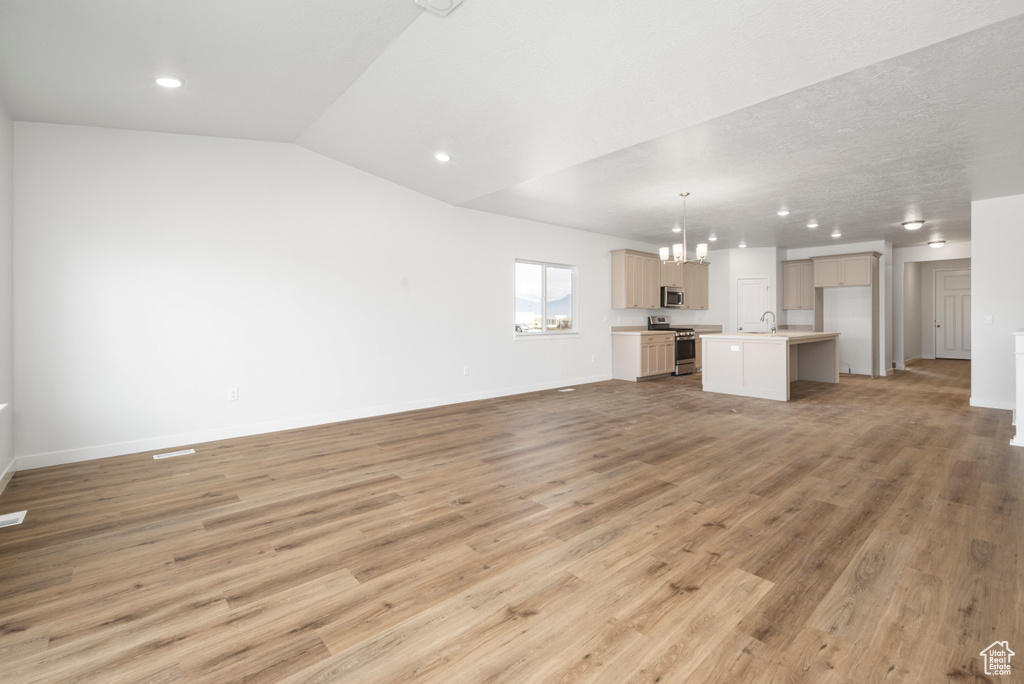 Unfurnished living room featuring sink, light hardwood / wood-style floors, lofted ceiling, and a chandelier