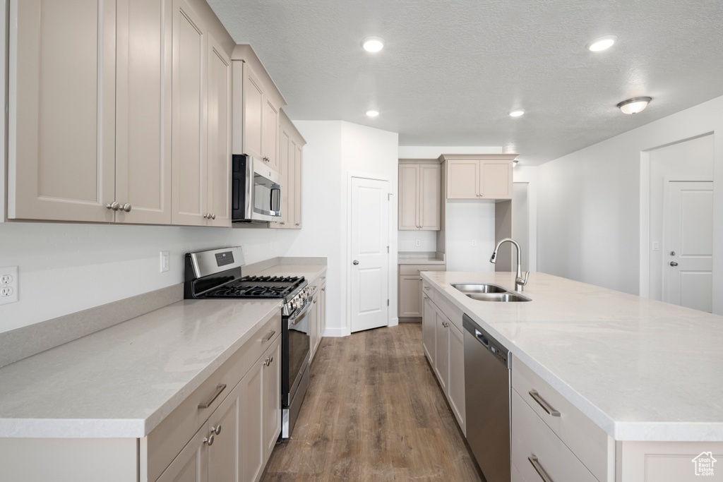 Kitchen with stainless steel appliances, hardwood / wood-style flooring, light stone countertops, an island with sink, and sink