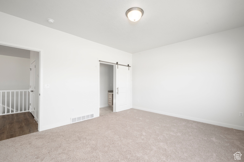 Unfurnished bedroom with a barn door and carpet floors