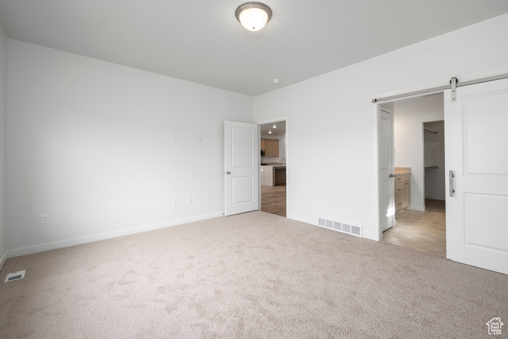 Unfurnished bedroom featuring carpet flooring, ensuite bathroom, and a barn door