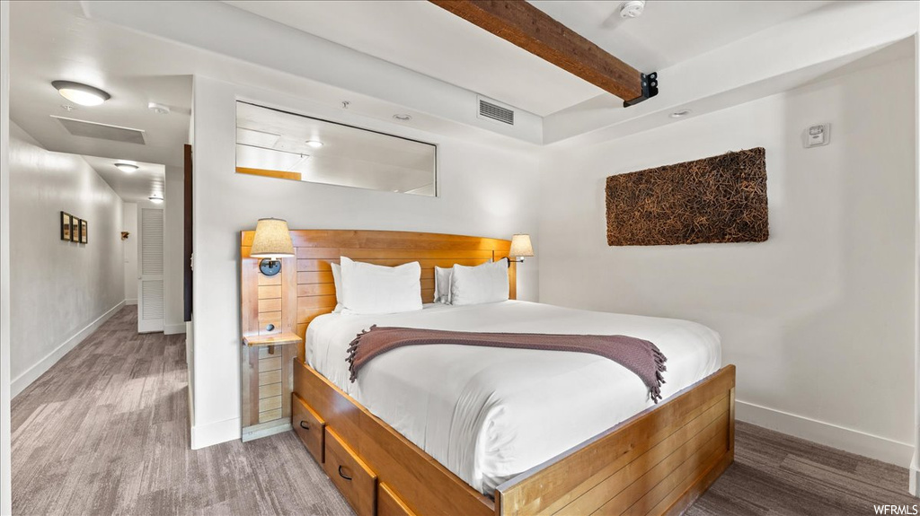 Hardwood floored bedroom featuring beam ceiling