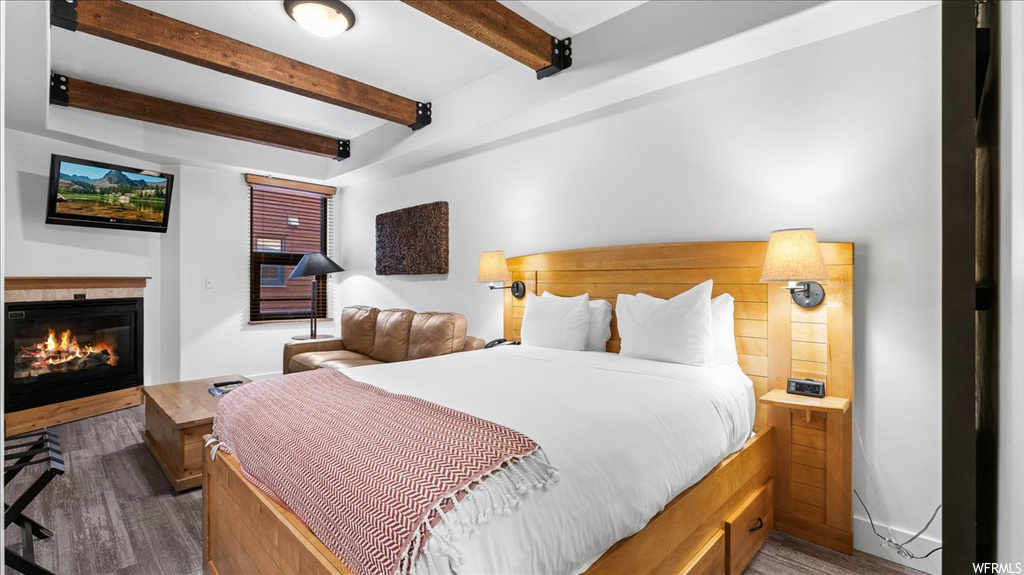 Hardwood floored bedroom featuring beam ceiling