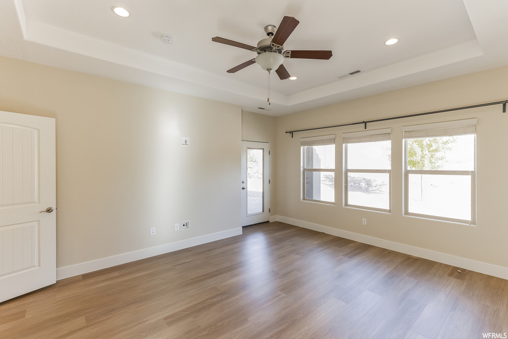 Spare room featuring a raised ceiling, light hardwood floors, and ceiling fan
