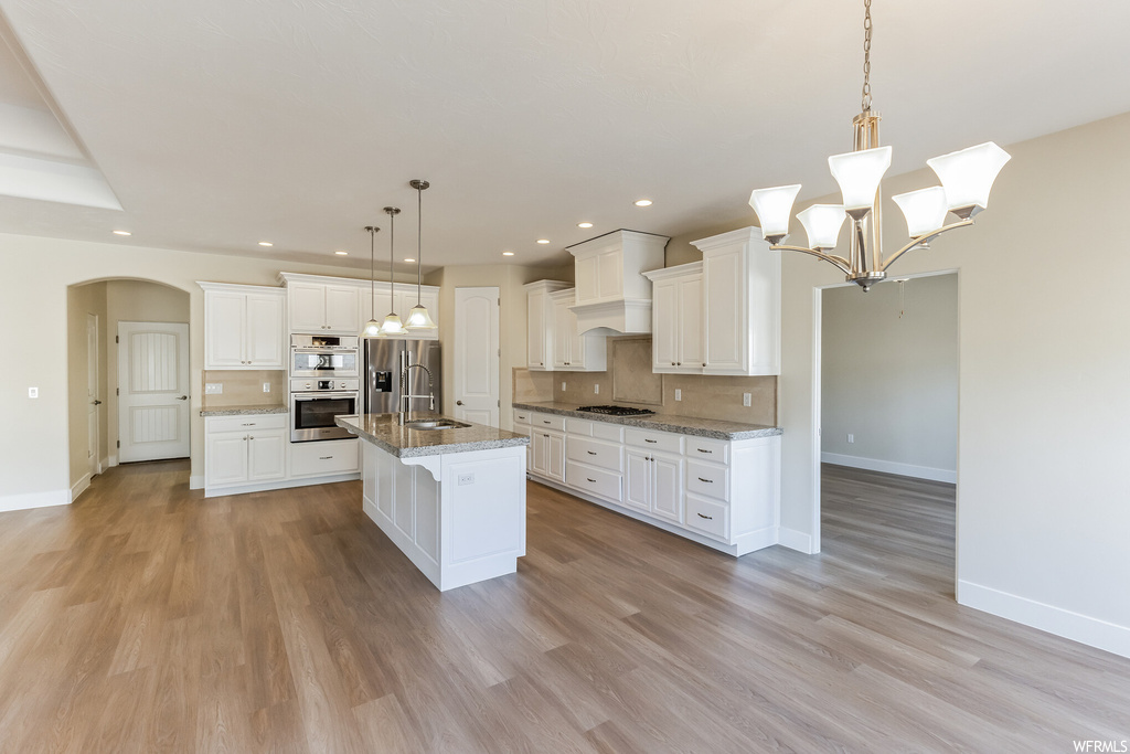 Kitchen with decorative light fixtures, a kitchen island with sink, light hardwood flooring, white cabinets, and a chandelier
