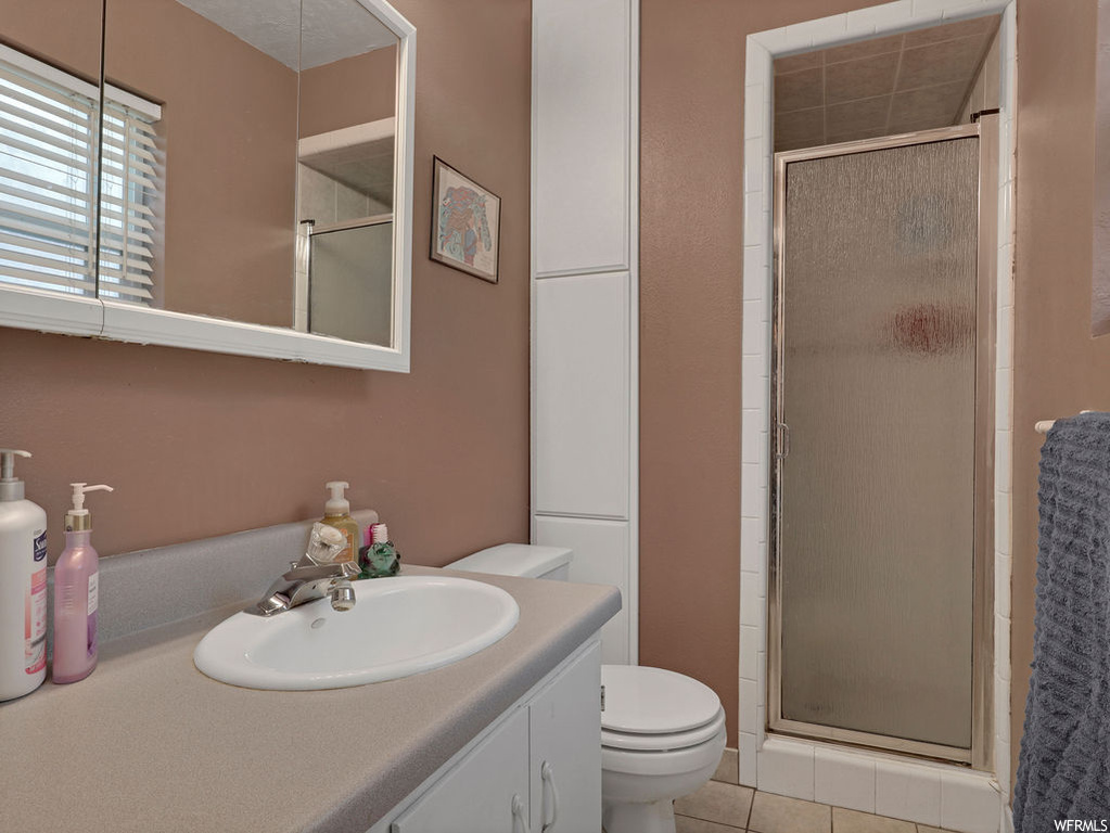 Bathroom featuring tile flooring, large vanity, toilet, and an enclosed shower
