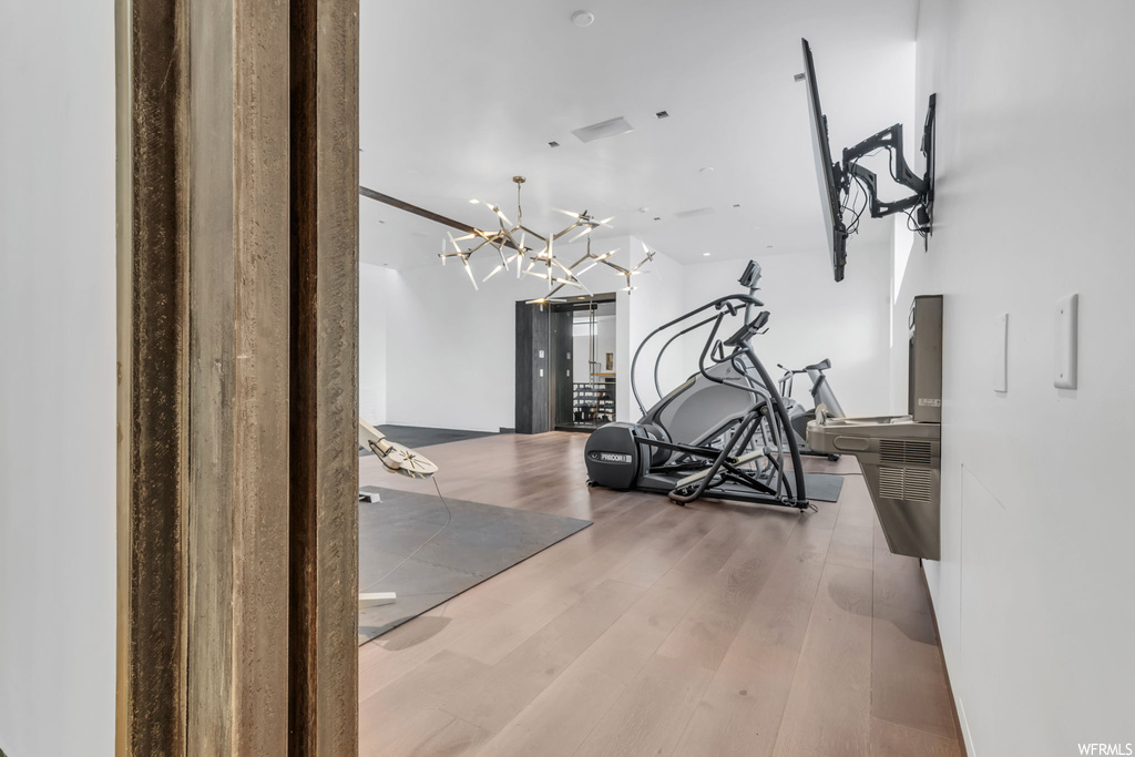 Exercise room featuring light hardwood floors and a chandelier