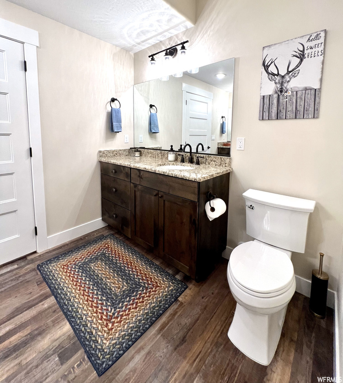 Bathroom featuring a textured ceiling, vanity, toilet, and wood-type flooring
