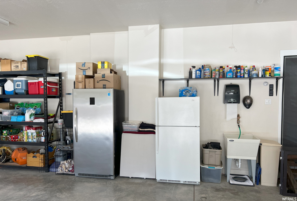 Kitchen featuring white fridge, concrete floors, white cabinets, and stainless steel refrigerator