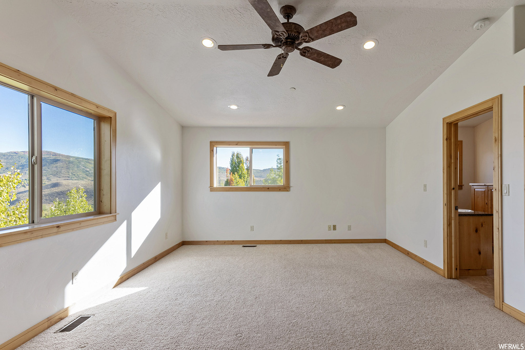 Carpeted empty room with vaulted ceiling, ceiling fan, and a wealth of natural light