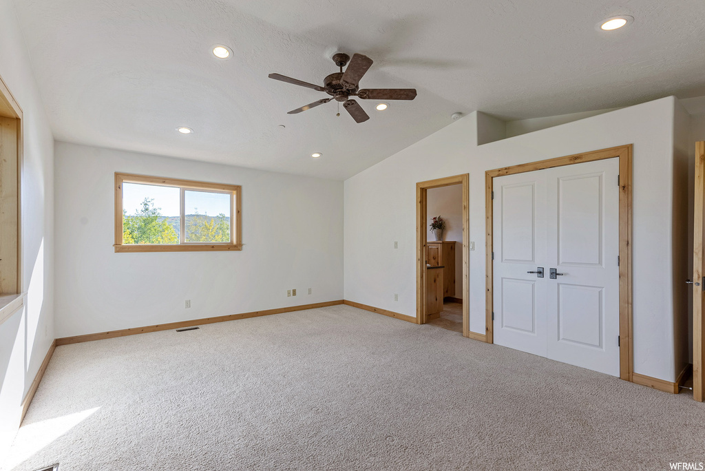 Unfurnished bedroom featuring light carpet, vaulted ceiling, and ceiling fan