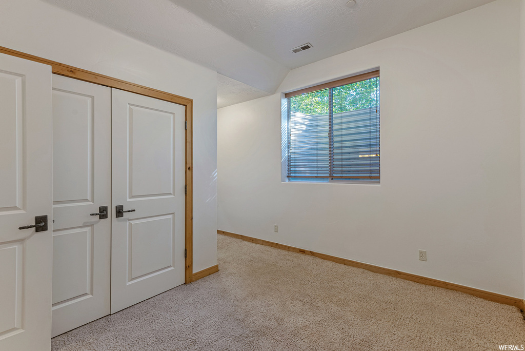 Unfurnished bedroom with light carpet, a closet, and lofted ceiling