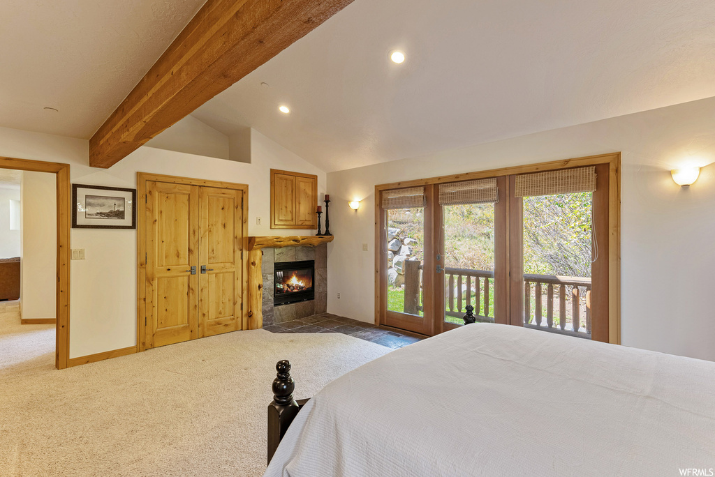 Carpeted bedroom featuring vaulted ceiling with beams, a fireplace, and access to outside