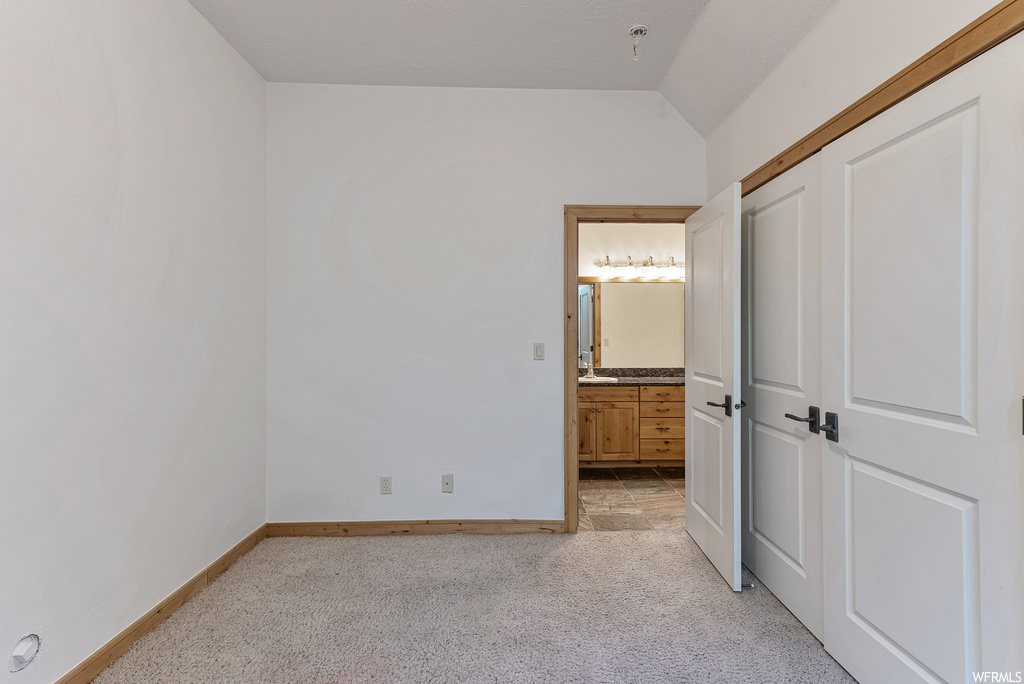 Unfurnished bedroom featuring ensuite bath, vaulted ceiling, a closet, and light colored carpet